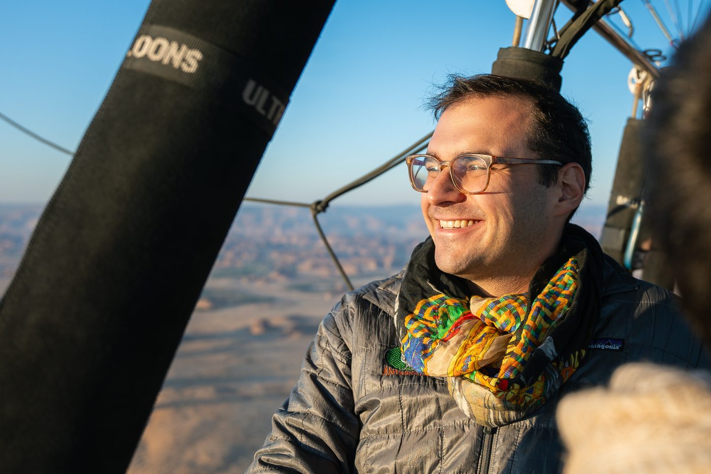Adam Starr smiling while riding in a hot air balloon over a desert landscape